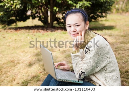 asian female sit in grass field with laptop