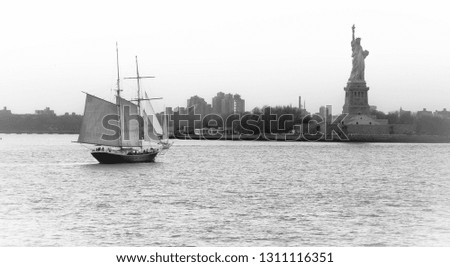 Panoramic view of American symbol Statue of Liberty in New York, USA, with sailing ship and boats sailing on the Hudson River. High key black and white image.