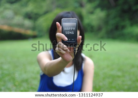 a young girl holding up a cell phone digital music player with the title "Happy Songs"