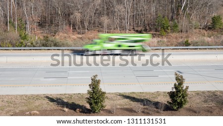 A green crane utility truck in blurred motion on a highway showing movement while the rest of the shot is in focus.