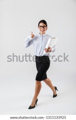 Full length photo of european businesswoman wearing eyeglasses holding paper folder in the office isolated over white background