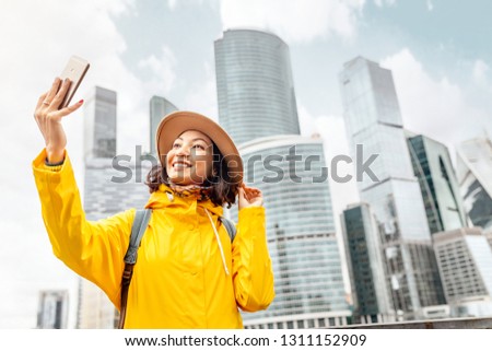 Happy travel asian girl tourist taking selfie photo by her smartphone on the background of a modern skyscraper city center downtown