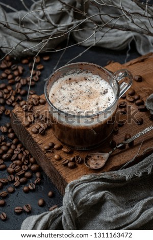 Coffee with milk foam on a wooden board and a scattering of coffee beans. Low key photography.