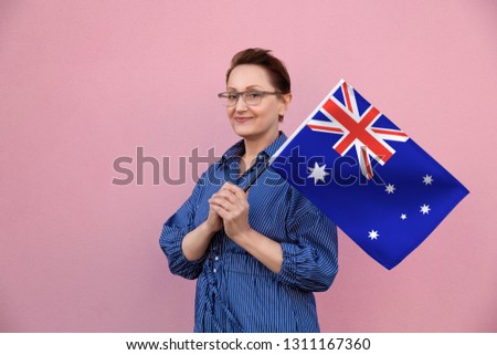 Australia flag. Woman holding Australian flag. Nice portrait of middle aged lady 40 50 years old holding a large flag over pink wall background on the street outdoors.