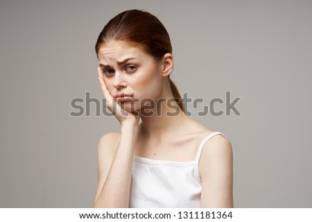 Sick woman holding hand on face in white t-shirt gray background health problems