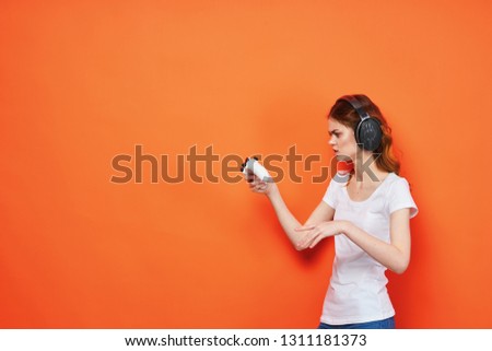 Pretty woman in headphones with a controller from the gaming console on an orange background