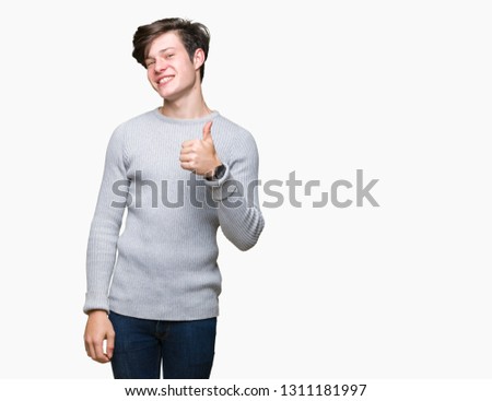 Young handsome man wearing winter sweater over isolated background doing happy thumbs up gesture with hand. Approving expression looking at the camera showing success.
