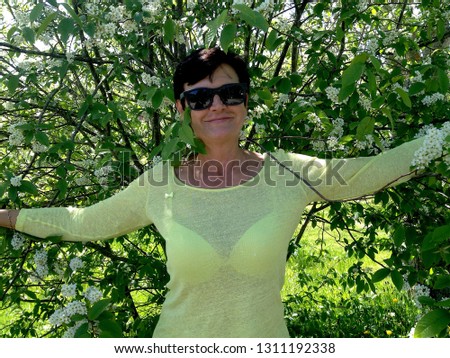 A woman stands in the shade of a large bush of cherry in the spring