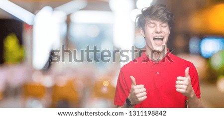 Young handsome man wearing red t-shirt over isolated background success sign doing positive gesture with hand, thumbs up smiling and happy. Looking at the camera with cheerful expression, winner