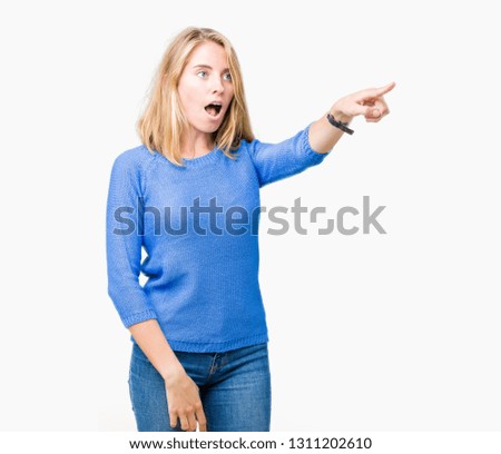 Beautiful young woman wearing blue sweater over isolated background Pointing with finger surprised ahead, open mouth amazed expression, something in front