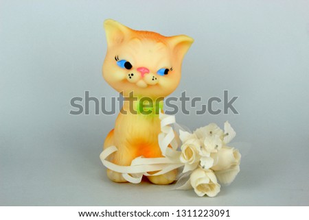 pretty toy kitten with a pink nose, with a green bow at the neck, next to a bouquet of white artificial flowers