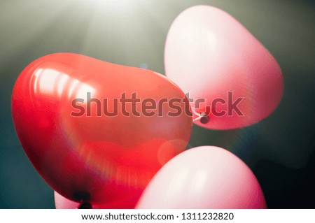 Motion blur, film grain effect, Vintage red pink balloons heart shape flying up through sun rays. Valentines romantic love concept. Soft focus close up image 
