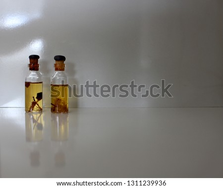 Two bottles of natural perfume, containing plants, on the left of the photo, on white background