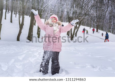 A happy girl playing with snow in a park, throwing snow upwards.