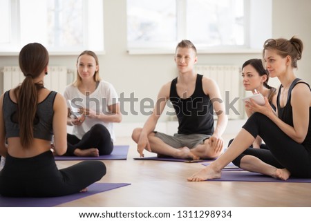 Millennial diverse people sit in circle at yoga workshop, write in notebooks listening to teacher or trainer, sporty men and women study at seminar at gym or training studio, becoming future coach Royalty-Free Stock Photo #1311298934