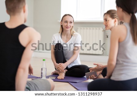 Millennial athletes sit on yoga mats in fitness studio talking after training, diverse sporty men and women chatting during break at gym sport session, fit people speak collaborating in room
