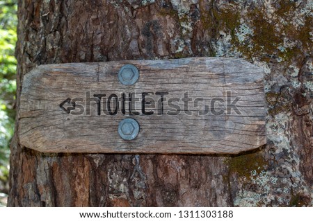 Wooden toilet sign bolted on a tree