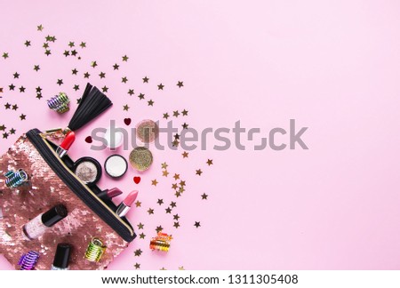Bright composition of fashion accessories. Glitter sequins cosmetic bag with lipsticks, nail polishes and other objects. Object on soft pastel background with decorative tinsel. Flat lay, top view