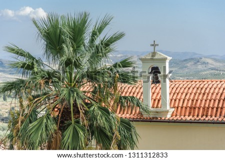 Tile roof of the monastery with an Orthodox cross and bell on the background of mountains and cloudy sky