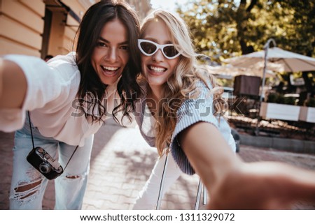 Fashionable latin girl making selfie with friend. Outdoor portrait of two cute ladies having fun together. Royalty-Free Stock Photo #1311329072