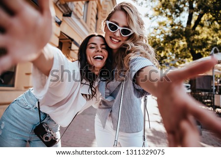 Excited young woman with camera spending weekend with friend. Outdoor shot of spectacular blonde girl making selfie in warm day.