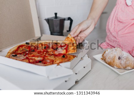 Photo of fast food on kitchen table. Indoor shot of woman eating pizza and croissant in morning.