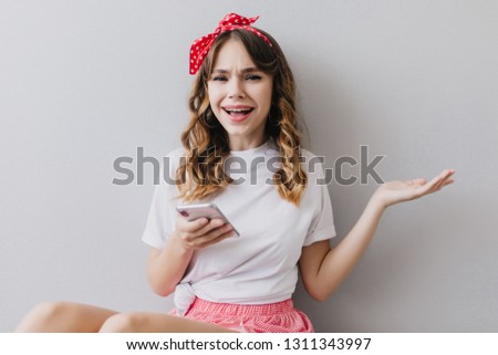 Funny young woman in casual outfit posing in her room with phone. Romantic white girl holding smartphone in hand.