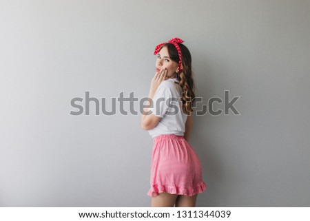 Portrait of romantic lady in pajamas looking over shoulder. Indoor photo from back of curly girl in pink shorts.
