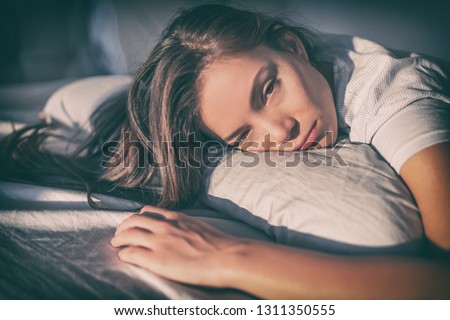 Tired woman lying in bed can't sleep late at night with insomnia. Asian girl with funny face sick or sad depressed sleeping at home. Royalty-Free Stock Photo #1311350555