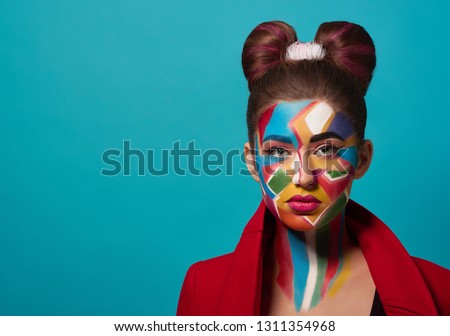 Portrait of funky girl with creative and colorful make up on face. Beautiful model wearing in red clothes, looking at camera, posing in studio. Woman has hairstyle bow, pink, plump lips.