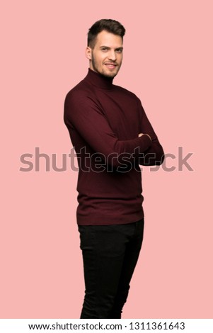 Man with turtleneck sweater with arms crossed and looking forward over pink background