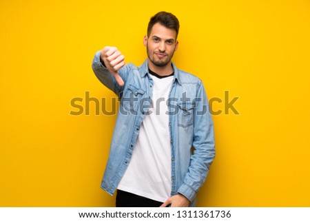 Handsome man over yellow wall showing thumb dowg with negative expression
