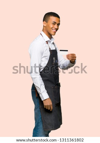 Young afro american barber man holding a credit card on isolated background