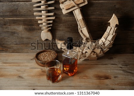 glass and bottle of whiskey with wheat in a bowl on the background of the anchor on a wooden oak background with copy space for text
