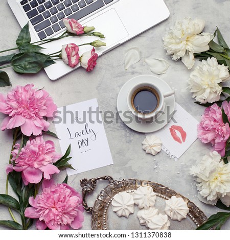 Flat lay with laptop, cup of coffee, flowers, meringues on a vintage tray and greeting card with "Lovely day" text on concrete background. Feminine blogger home office desk. Overhead view