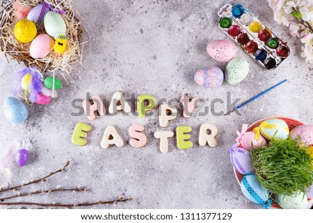 Easter eggs in a nest of grass, homemade glazed cookies and paints for painting eggs and grass as attributes of the preparation of the Easter holiday on a stone background, flat lay