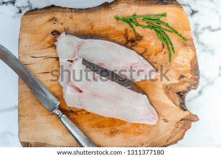 Two raw halibut steaks on wooden board garnished with samphire - top view