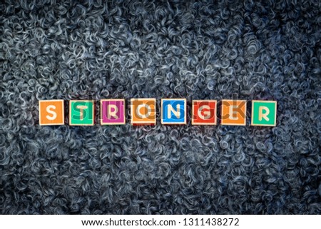 The word STRONGER written with colorful wooden block letters on a sheepskin. The word is placed in the middle.
