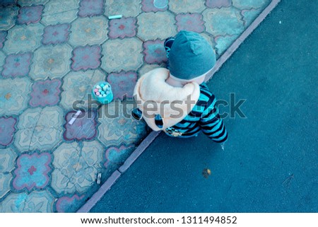 a litle boy drawing with chalk on asphalt, bucket with crayons of different colors