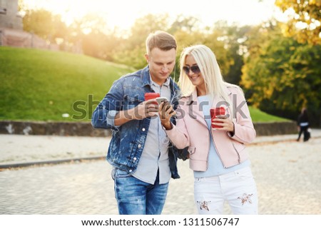 Smiling couple in love walking in autumn park, holding hands. Listen to music on headphones and drink coffee to go. Have a fun together. Hugging and kissing 