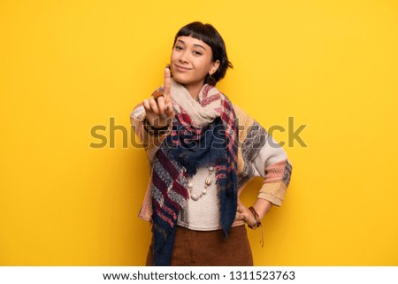 Young hippie woman over yellow wall showing and lifting a finger