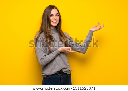 Young woman over yellow wall extending hands to the side for inviting to come