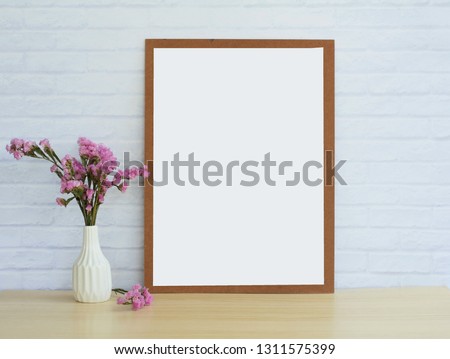 Mock up of the white of the picture frame placed on a wooden table and with a white vase, background, white brick wall