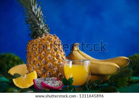 Tropical fruits fresh juice on a blue background with bananas, pineapple, mango and dragon fruit. Exotic drink header with copy space