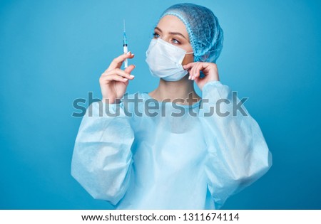 surgeon in a medical mask with a syringe on a blue background                            