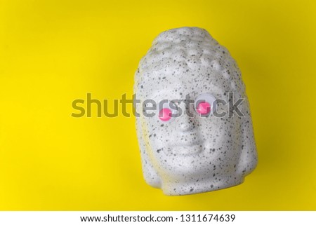 Buddha ceramic head with pink googly eyes on a yellow background