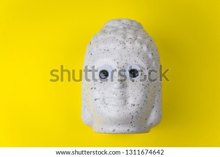 Buddha ceramic head with googly eyes on a yellow background