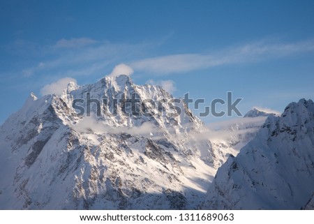 mountain peaks of Dombai mountains covered with snow surrounded by thick clouds against the blue sky. February 2019