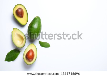 Minimal composition with whole and halved nutrient dense avocado fruit slices full of heart healthy monounsaturated fat on gray glass table top. Close up, copy space, top view, background. Royalty-Free Stock Photo #1311716696
