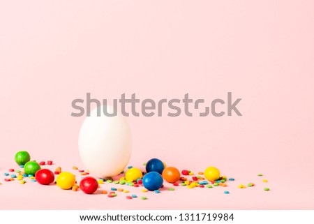 White Easter egg and multi-colored sweets on a pink background. Easter celebration concept.